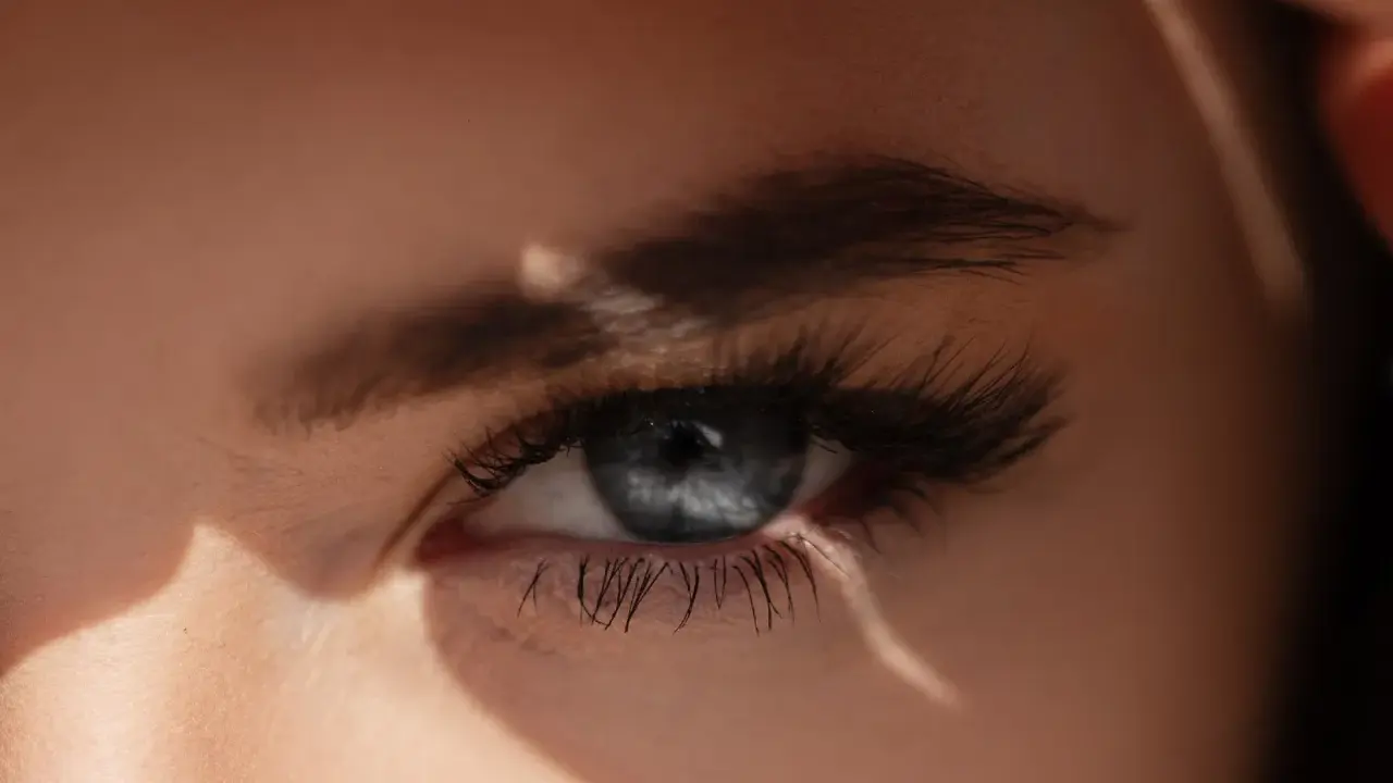 Un œil bleu intense, sublimé par un microblading parfait, capte la lumière du soleil.