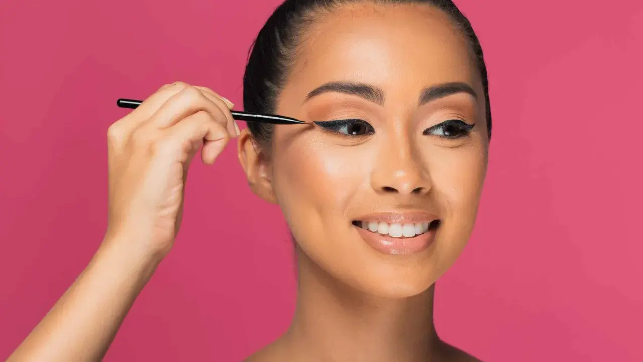 Une femme crée des "siren eyes" avec un eye-liner précis, son regard captivant promettant une beauté envoûtante.