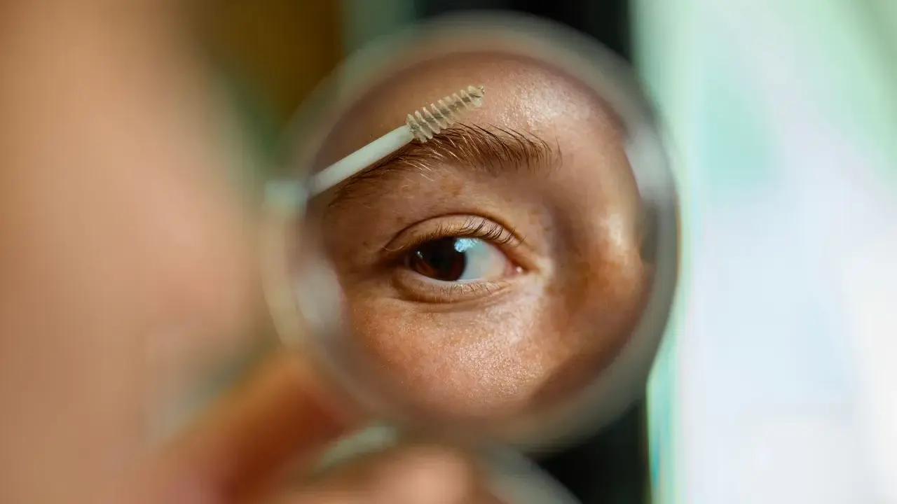 Gros plan sur un œil et un sourcil, une brosse à sourcils est utilisée pour les coiffer. La question est : est ce que les sourcils repoussent ?