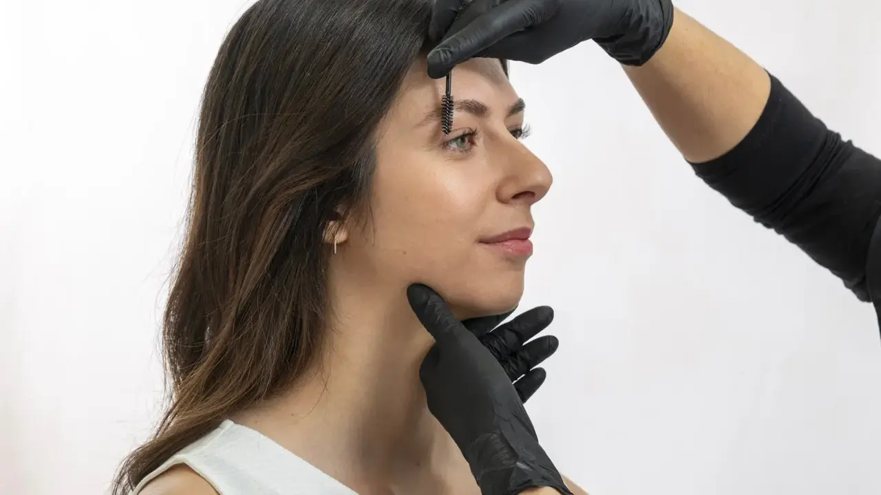 Une esthéticienne ajuste les sourcils d'une femme avec une brosse, préparant un browlift pour un regard sublimé.