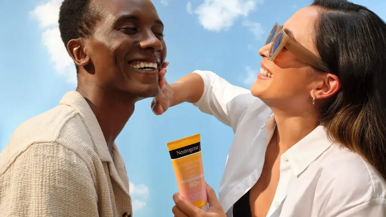 Un homme rit sous le soleil, une femme lui applique de la crème solaire pour protéger son visage.
