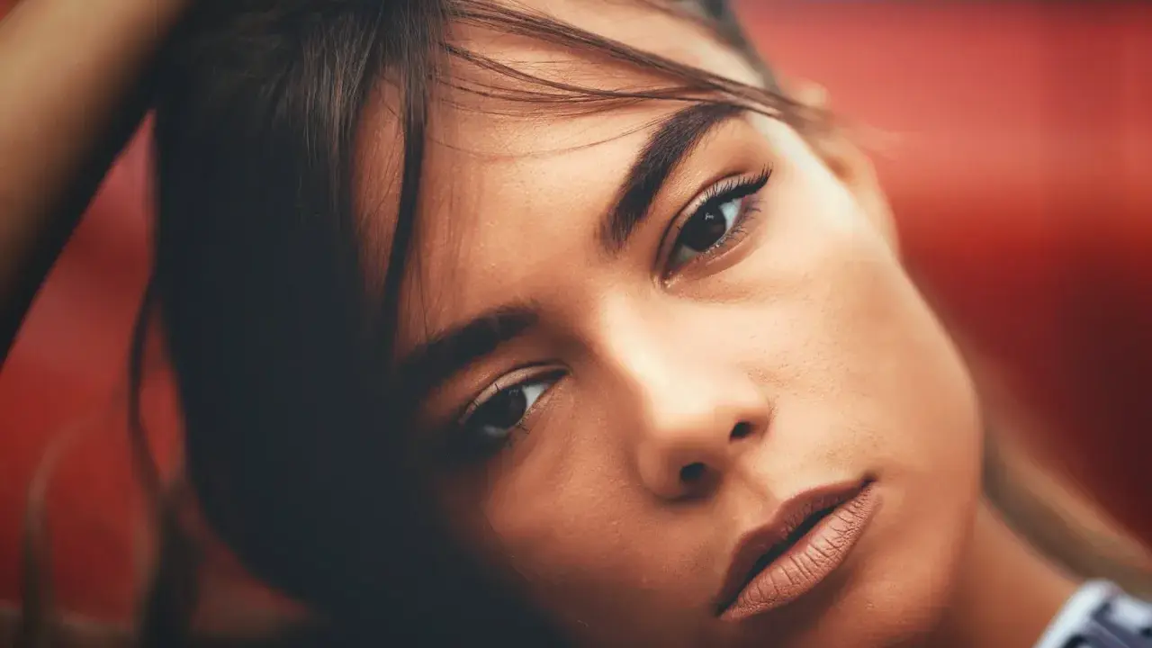 Portrait d'une jeune femme aux gros sourcils, la main dans les cheveux, regard intense.