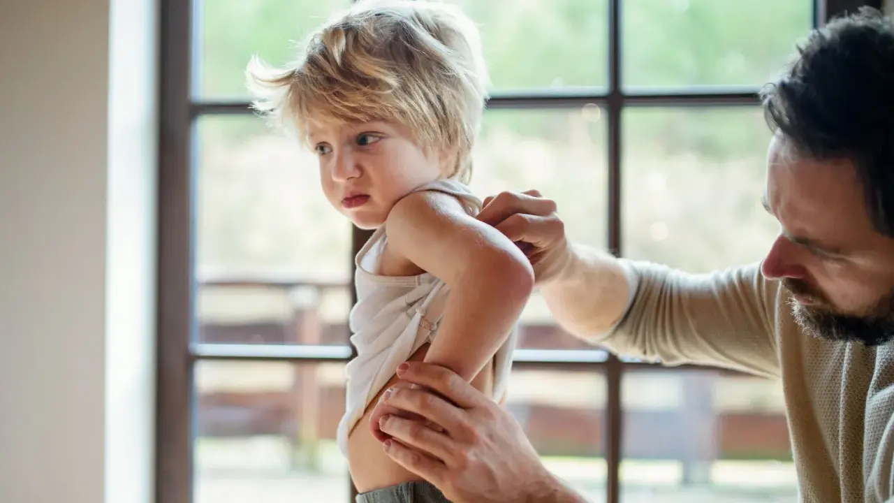 Un père examine le dos de son enfant, peut-être pour vérifier une poussée d'eczéma.