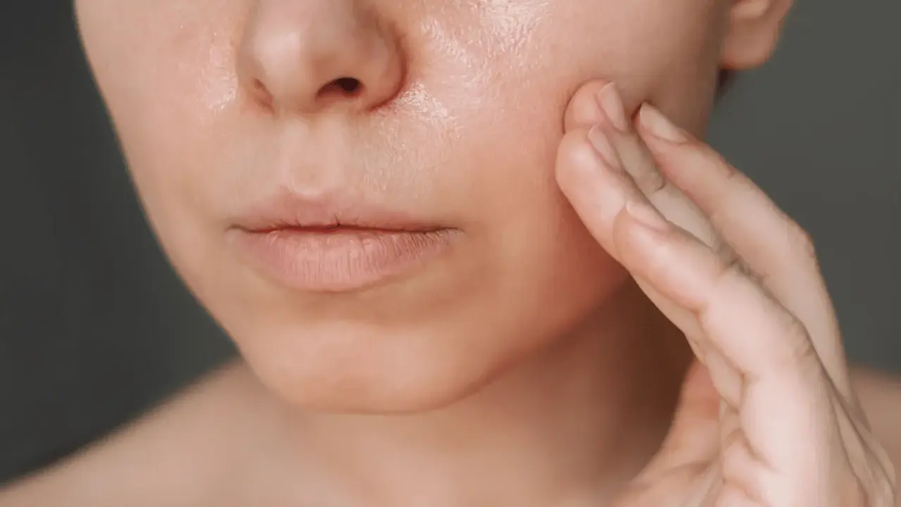 Une main touche délicatement la joue d'une femme, révélant une peau lumineuse, idéale pour une routine peau grasse.