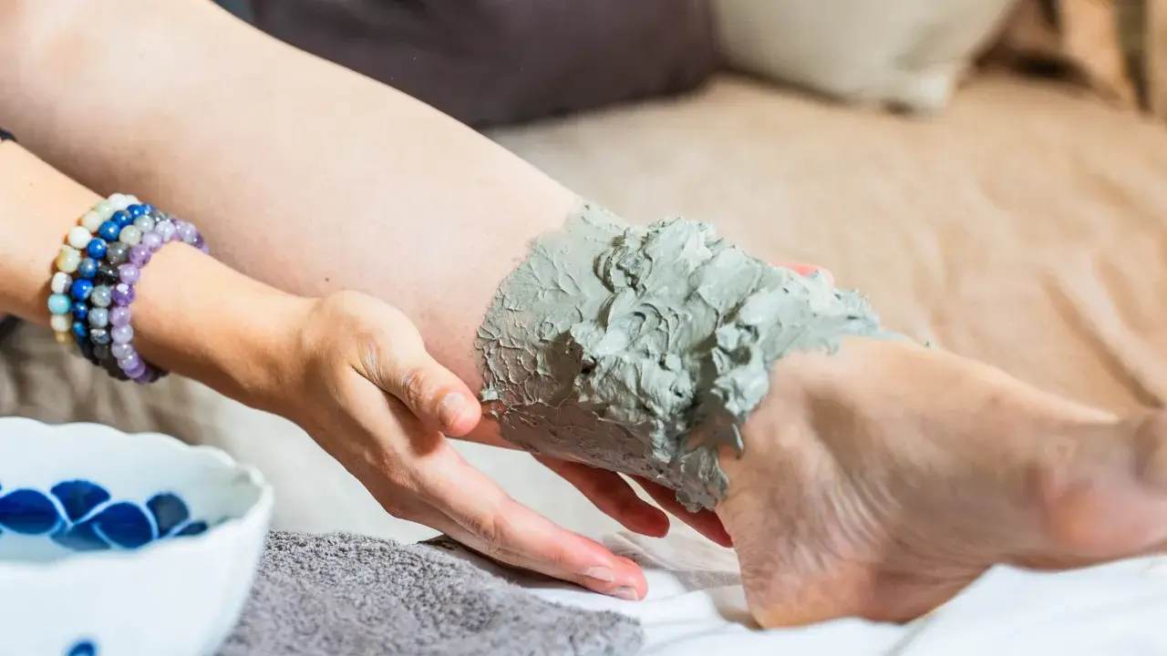 Application d'un cataplasme d'argile verte sur une jambe, pour un soin détoxifiant et apaisant.