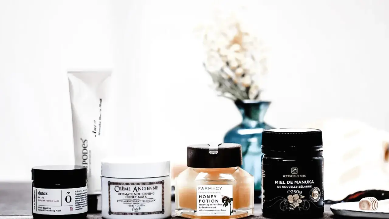 Plusieurs masques pour le visage, dont un masque au miel, sont disposés sur une table en bois.