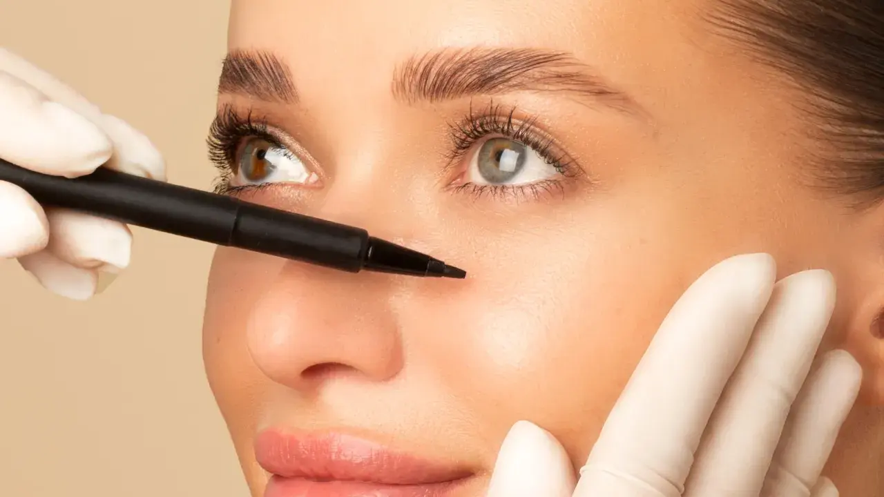 Une main gantée utilise un stylo pour marquer le visage d'une femme, préparant un brow lift pour un regard plus jeune et lifté.