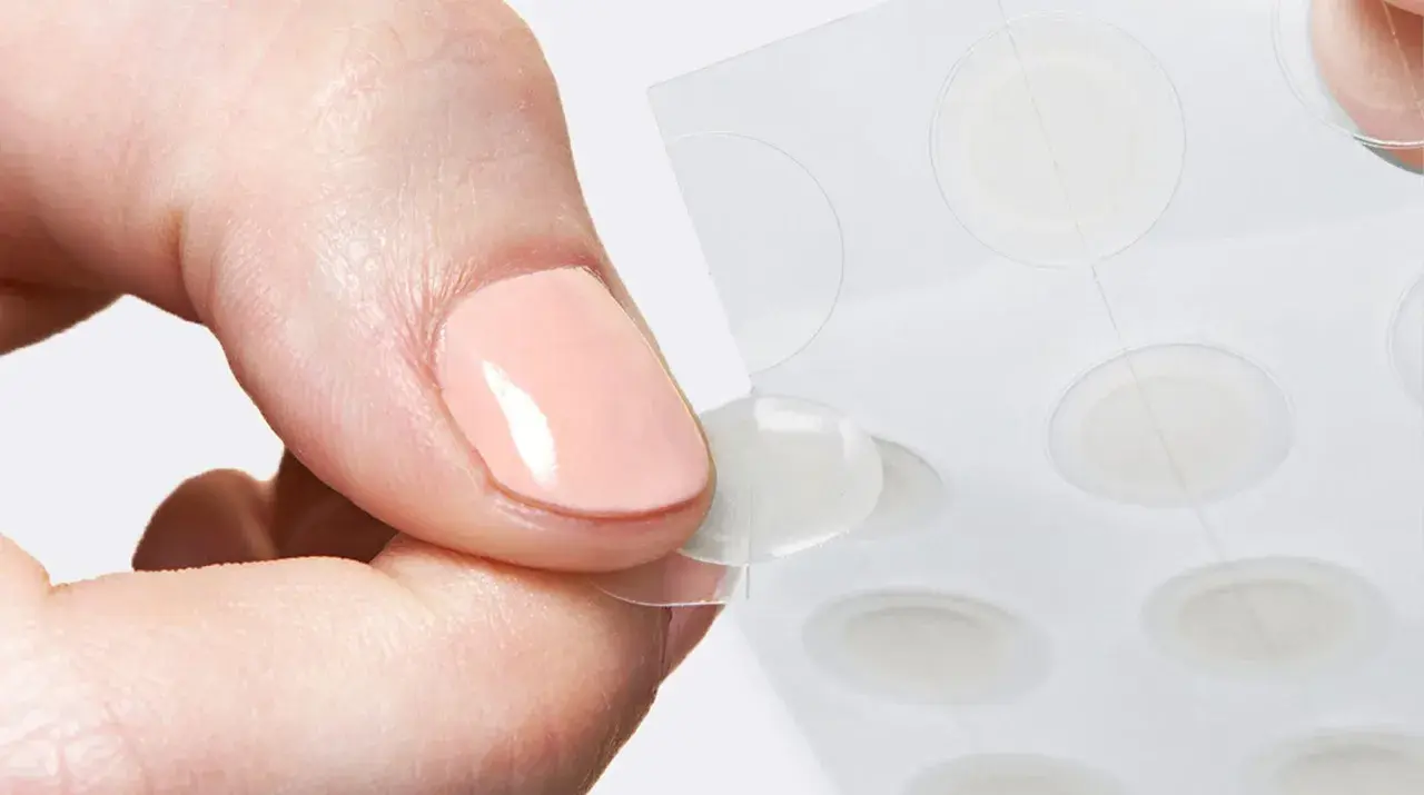 Une main retire délicatement un patch boutons d'une feuille, prêt à agir contre les imperfections.