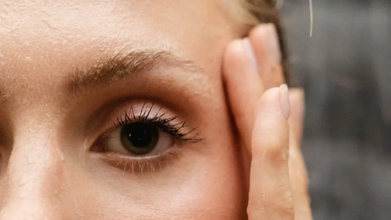 Un œil attentif, cils longs, et le début du repousse sourcils après chimio. Une main effleure le visage.