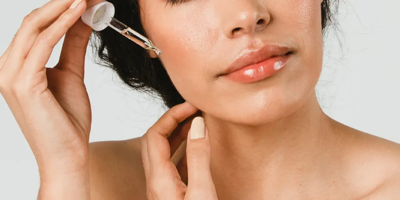 Une main applique une goutte d'huile de ricin visage sur la peau. Les lèvres sont brillantes, la peau est lumineuse.