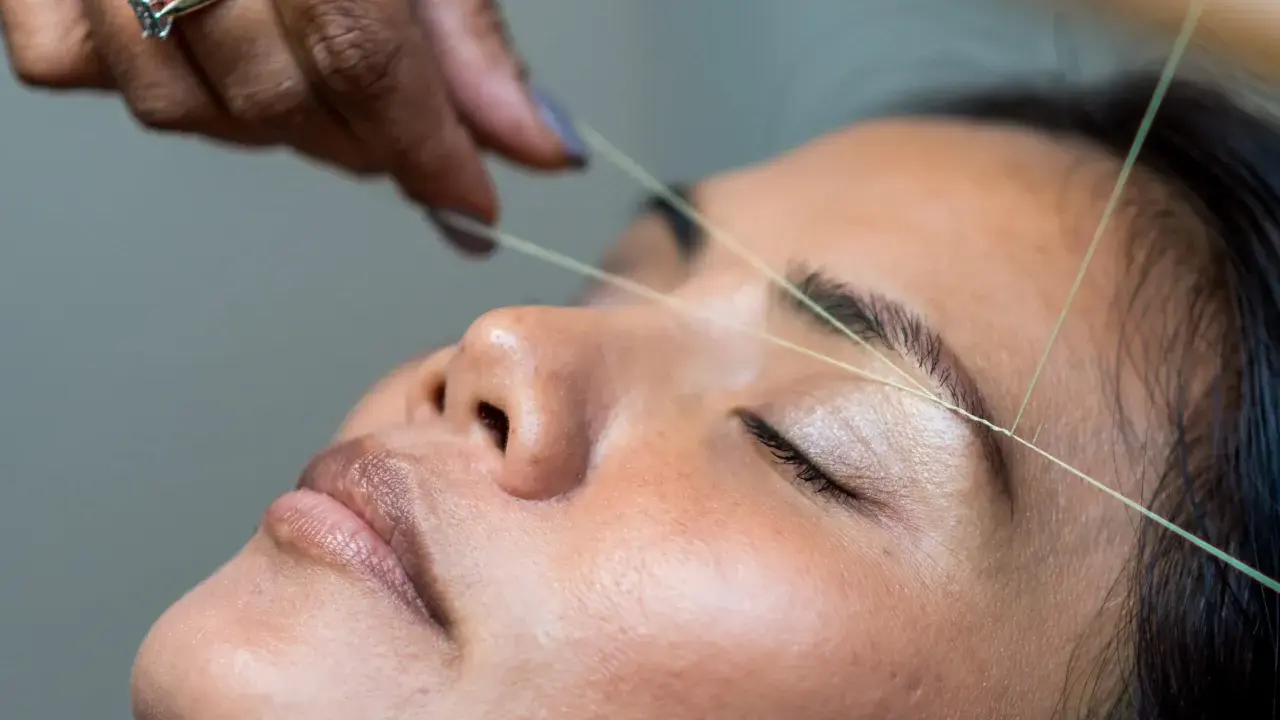 Une main utilise un fil pour épiler ses sourcils.