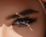 Un œil bleu intense, sublimé par un microblading parfait, capte la lumière du soleil.
