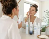 Une femme applique de l'eau thermale Avène sur son visage, entourée d'autres brumisateurs d'eau thermale.
