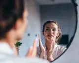 Une femme se regarde dans un miroir, appliquant de la mousse sur son visage pour un double nettoyage.