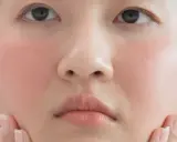 Gros plan sur le visage d'une jeune femme, ses joues légèrement rosées, un léger rougissement sur son visage rouge. Ses mains effleurent délicatement ses joues.