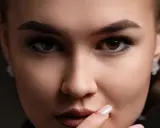 Gros plan sur un visage féminin aux **sourcils droits** et maquillés. Elle porte des boucles d'oreilles discrètes.