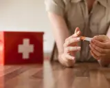 Une personne applique un pansement sur son doigt, près d'une trousse de secours rouge. L'objectif est une cicatrisation rapide.
