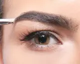 Une pince à épiler retire délicatement un poil du sourcil, affinant la ligne pour un regard parfait.