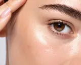 Gros plan sur un œil et un sourcil, la peau présente des taches et des cernes creuses, une main effleure le front.
