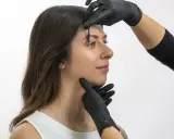 Une esthéticienne ajuste les sourcils d'une femme avec une brosse, préparant un browlift pour un regard sublimé.