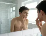 Un adolescent examine son visage dans le miroir, préoccupé par son acné.