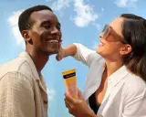 Un homme rit sous le soleil, une femme lui applique de la crème solaire pour protéger son visage.