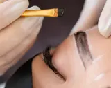 Application d'une teinture sourcils en institut. Un pinceau fin dépose la couleur sur un sourcil soigneusement dessiné.