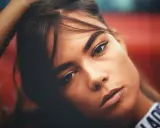 Portrait d'une jeune femme aux gros sourcils, la main dans les cheveux, regard intense.