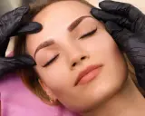 Une esthéticienne ajuste délicatement les sourcils d'une cliente lors d'une séance de dermopigmentation. Les sourcils sont parfaitement dessinés, offrant un regard sublimé.