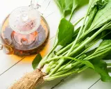 Thé infusé dans une théière en verre à côté de plantain frais, évoquant les bienfaits de cette plante.