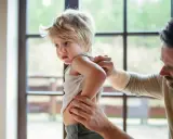 Un père examine le dos de son enfant, peut-être pour vérifier une poussée d'eczéma.