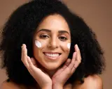 Une femme souriante applique du beurre de karité visage sur ses joues. Ses mains caressent doucement sa peau.