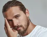 Un homme pensif, sa main effleurant son front, un sourcil plus haut que l'autre, regard intense.