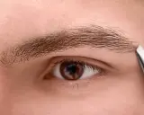 Un homme utilise une pince à épiler pour tailler un sourcil qui rebique, affinant son regard.