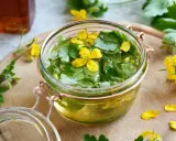 Un bocal rempli de chélidoine verrue, ses feuilles vertes et fleurs jaunes flottant dans un liquide doré. Une préparation naturelle pour prendre soin de sa peau.