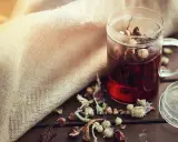 Infusion rouge dans une tasse en verre, entourée d'herbes séchées. Un remède naturel diurétique à portée de main.