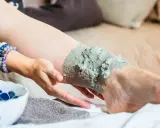 Application d'un cataplasme d'argile verte sur une jambe, pour un soin détoxifiant et apaisant.