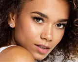 Un gros plan sur le visage d'une jeune femme aux cheveux bouclés, portant une boucle d'oreille étincelante. Ses **rehaucils avis** sont subtils, accentuant son regard.