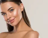 Visage d'une femme au teint hâlé, avec des yeux bleus et des lèvres roses. Elle sourit légèrement, suggérant une peau parfaite pour comment bronzer rapidement.