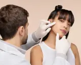Un médecin examine le visage d'une jeune femme, suggérant une consultation pour une pilule contre l'acné.