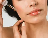Une main applique une goutte d'huile de ricin visage sur la peau. Les lèvres sont brillantes, la peau est lumineuse.