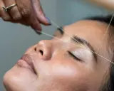 Une main utilise un fil pour épiler ses sourcils.