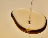 Un filet d'huile de karanja, d'une couleur ambrée, tombe sur une surface liquide, créant des reflets sombres. Attention, l'huile de karanja peut présenter un danger.