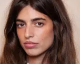 Portrait d'une jeune femme aux longs cheveux bruns. Son maquillage met en valeur ses yeux et ses lèvres, avec un soin particulier apporté à son sourcil poil à poil.
