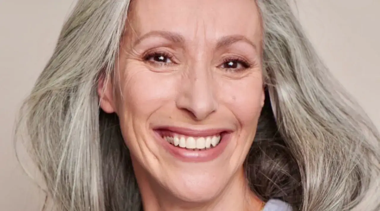 Visage souriant d'une femme aux cheveux gris, montrant comment cacher les cernes avec un maquillage naturel.