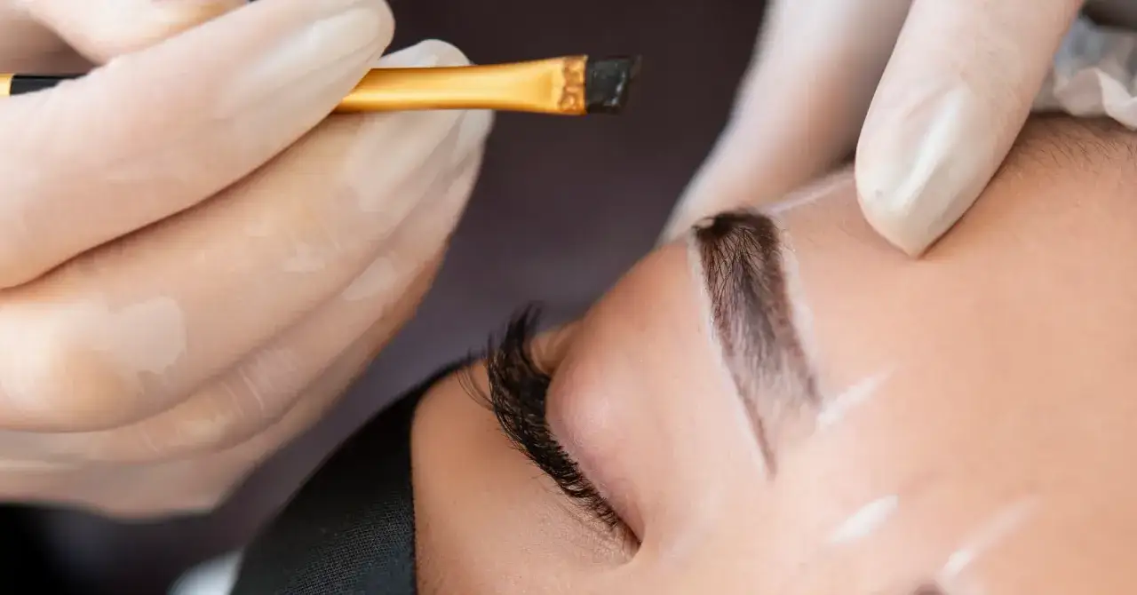 Application d'une teinture sourcils en institut. Un pinceau fin dépose la couleur sur un sourcil finement dessiné.