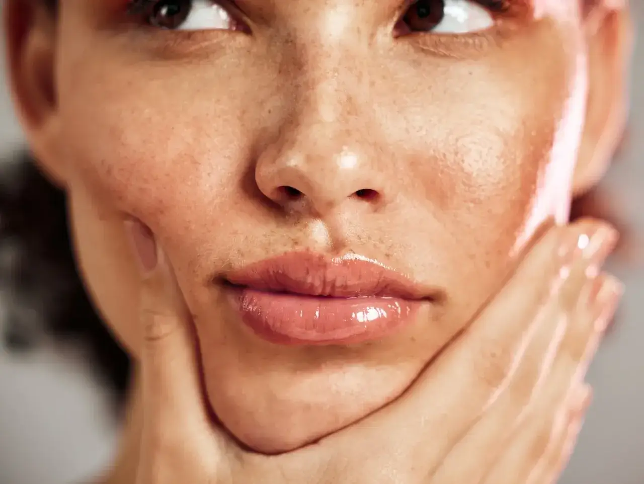 Gros plan sur le visage d'une femme, mettant en valeur sa peau lumineuse et ses taches de rousseur naturelles. Sa main caresse doucement sa joue.
