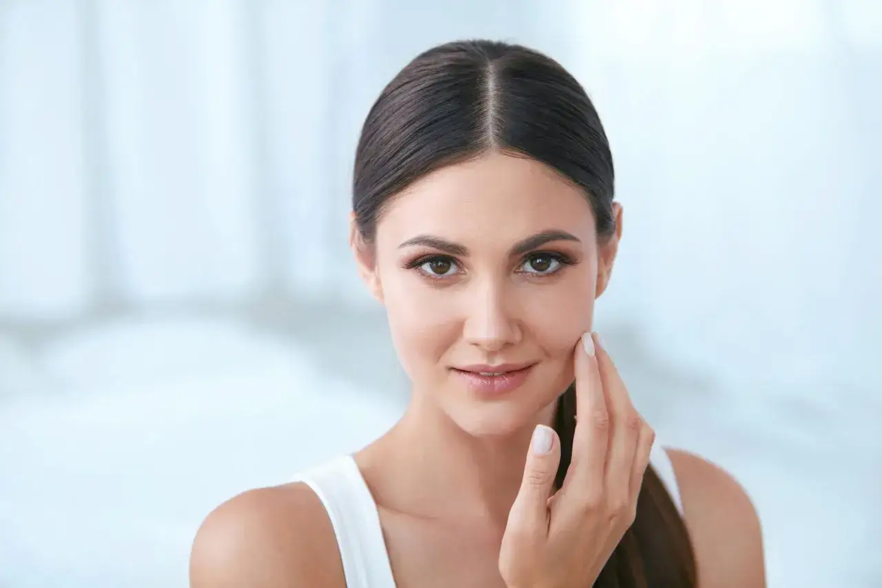 Une femme touche sa joue, sa peau est lisse et lumineuse. Est-ce que le maquillage abîme la peau ? Une question que beaucoup se posent.