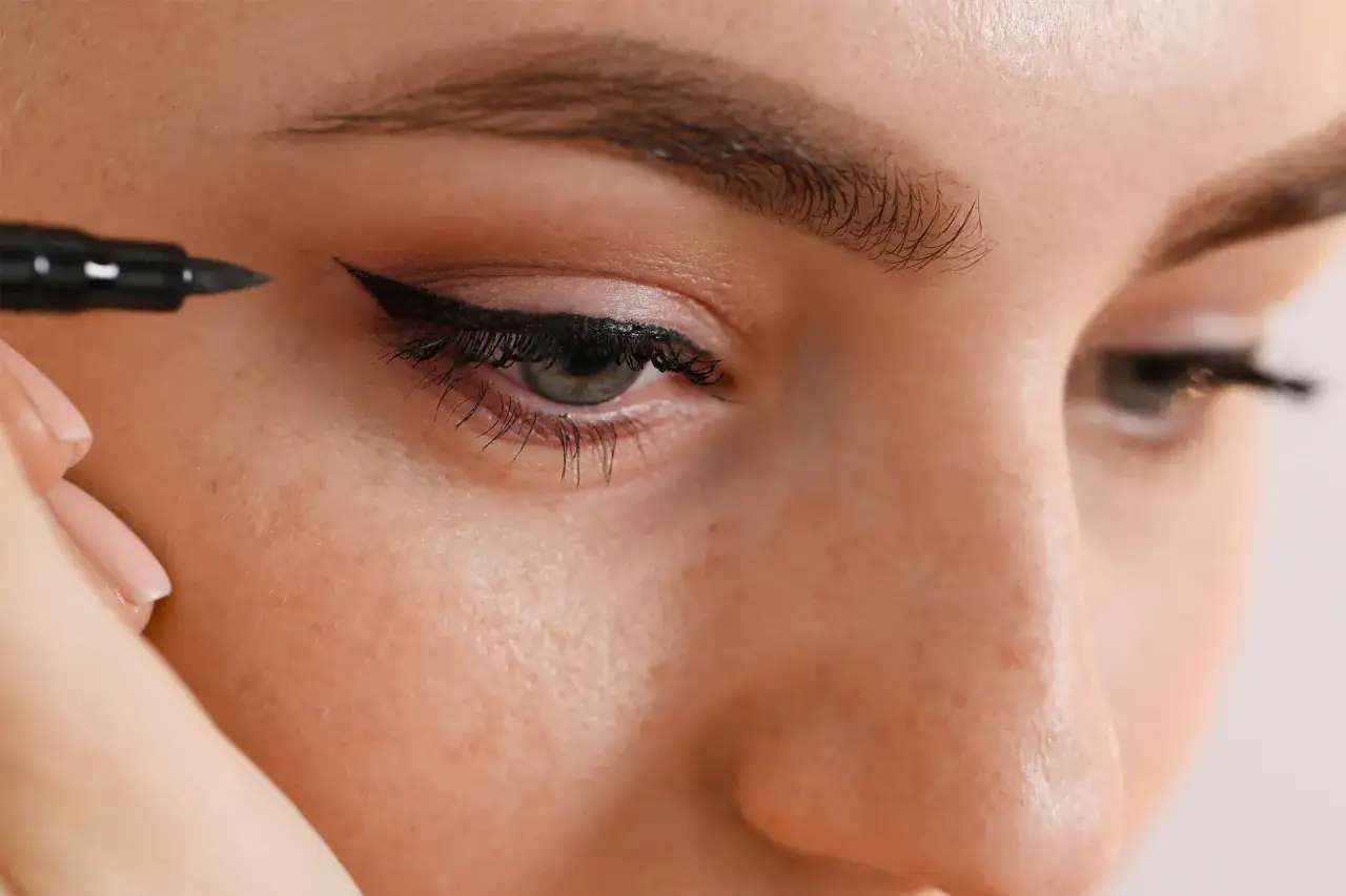 Application d'un trait d'eye-liner précis, étape vers un maquillage permanent yeux impeccable.