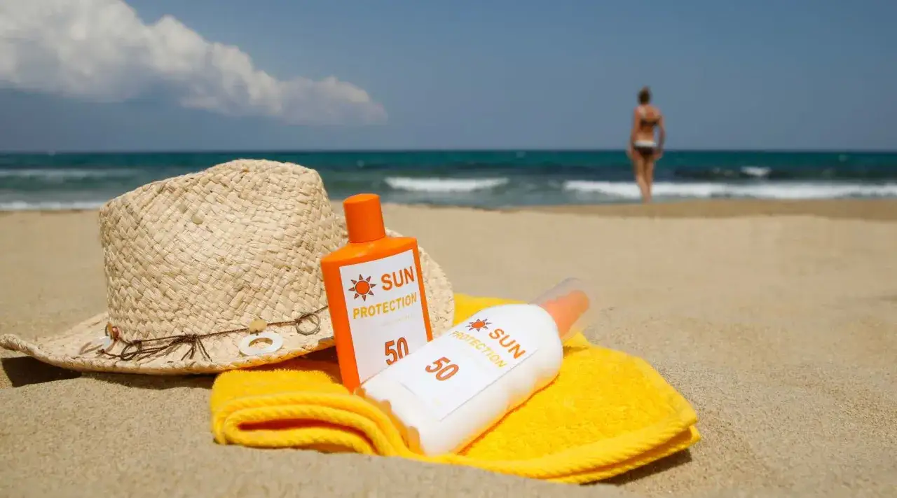 Chapeau de paille, serviette jaune et deux crèmes solaires SPF 50 sur le sable. La clé pour comment bronzer sans coup de soleil.